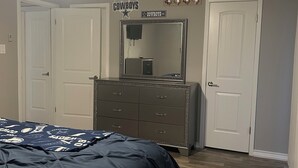 A bedroom with a bed, dresser, ceiling fan, and a sign on the wall. - Cozy & Comfortable in walking distance to AT&T, near Sixflags (Arlington)