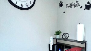 A corner with a wall clock, a coffee-themed wall decal, and a metal shelf with various items. - Cozy & Comfortable in walking distance to AT&T, near Sixflags (Arlington)