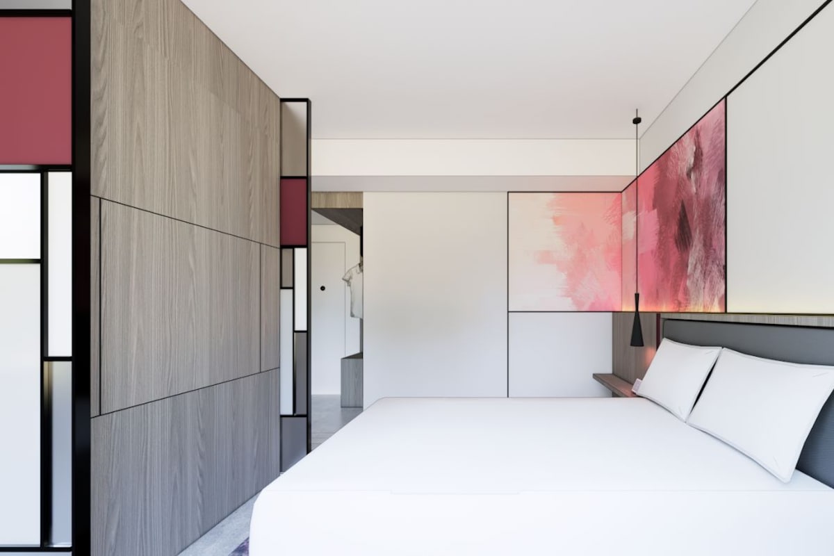A modern bedroom with a large bed, a nightstand, and a wall-mounted lamp.