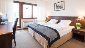 Hotelkamer met een bed, bureau, stoel en een raam met uitzicht op gebouwen en een vogel.