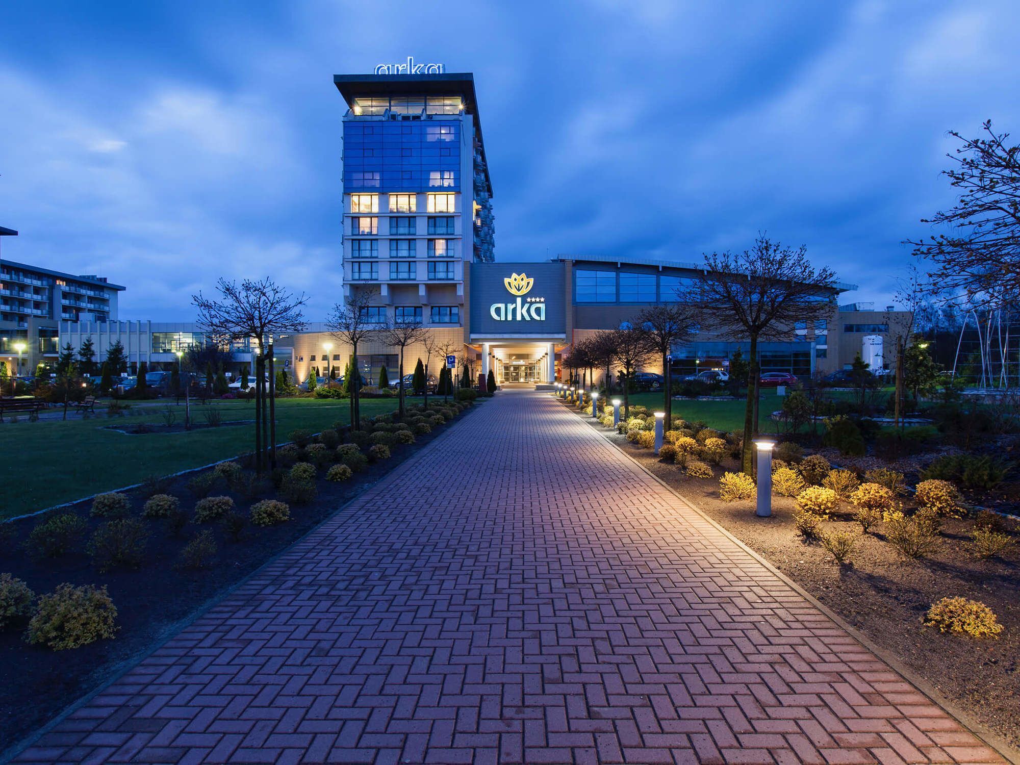 A hotel entrance with a paved pathway leading to the building, surrounded by landscaped areas and trees.