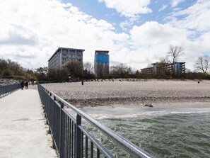 A coastal walkway with a metal railing, a sandy beach, and buildings in the background.