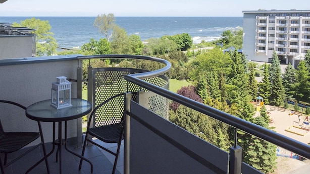 Een balkon met een tafel en stoelen, met uitzicht op een waterpartij en een park met speeltoestellen.