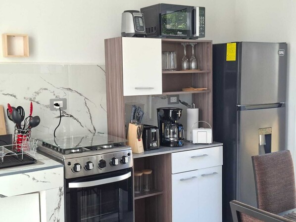 A compact kitchen with a stove, microwave, coffee maker, and refrigerator.