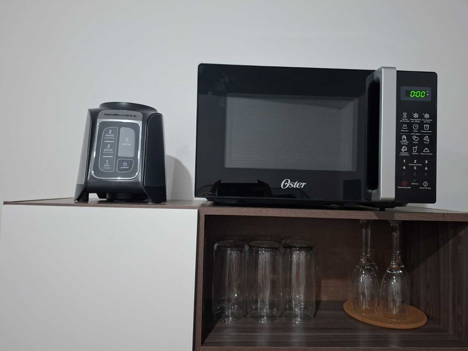En mikrovågsugn och en kaffebryggare står på en hylla, och under hyllan finns glasvaror.