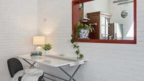 A compact room with a white desk, a chair, a mirror, a potted plant, and a hanging light fixture. - Pip's Cottage - Pets Friendly, Cafes, Bars, Jetty Beach (Coffs Harbour)