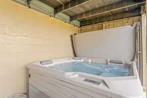 Een hottub met bedieningspaneel, voor een beige muur met een metalen dak.