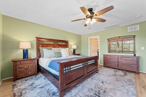 Une chambre à coucher comprenant un lit, des tables de chevet, une commode, un ventilateur de plafond et une fenêtre.