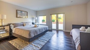 A bedroom with a large bed, a nightstand, a lamp, a framed picture, and a sliding glass door leading to an outdoor area. - Villa II Palazzo by Glam Homes (North Miami)