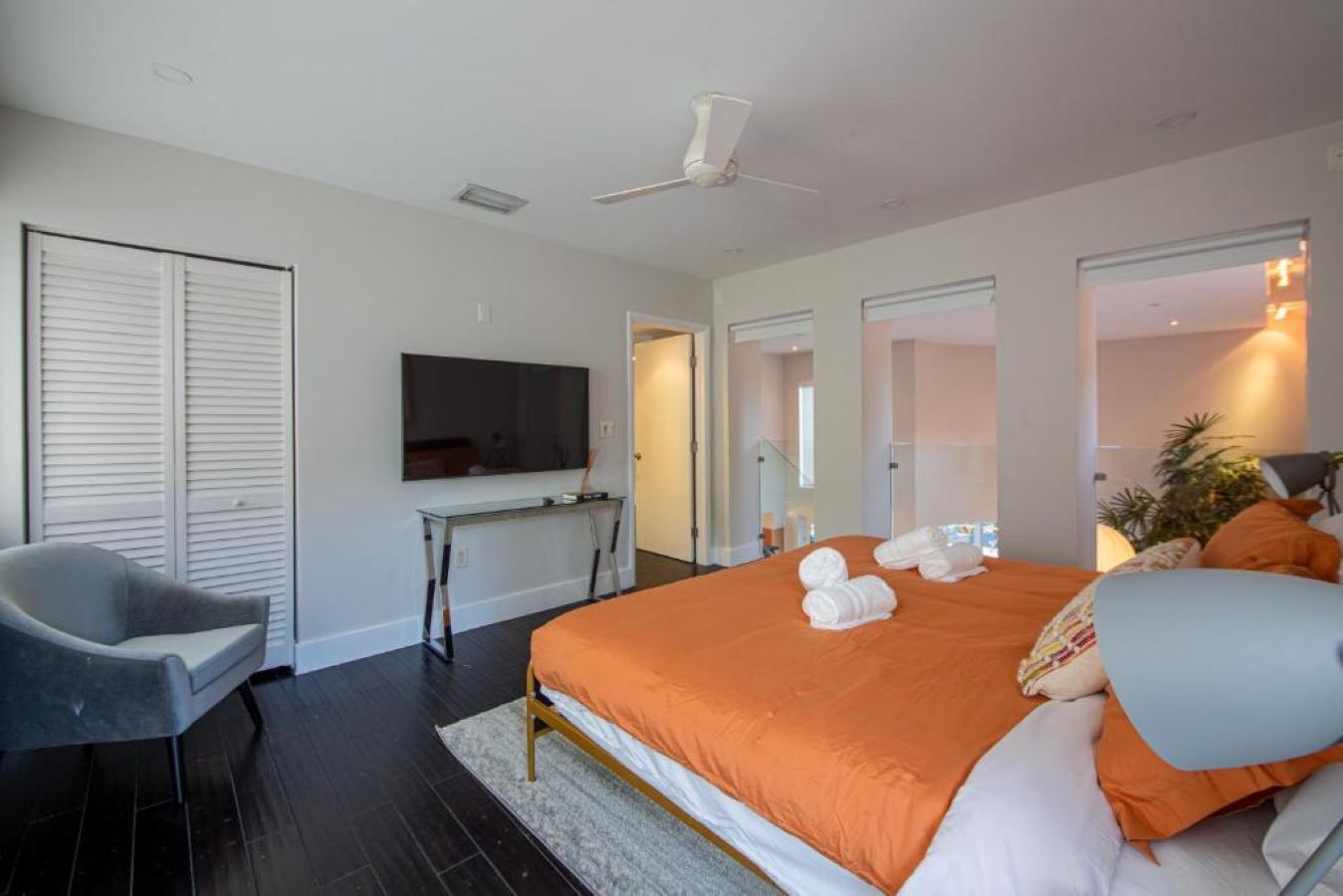 A modern hotel room with a bed, a desk, a chair, a television, and a ceiling fan.