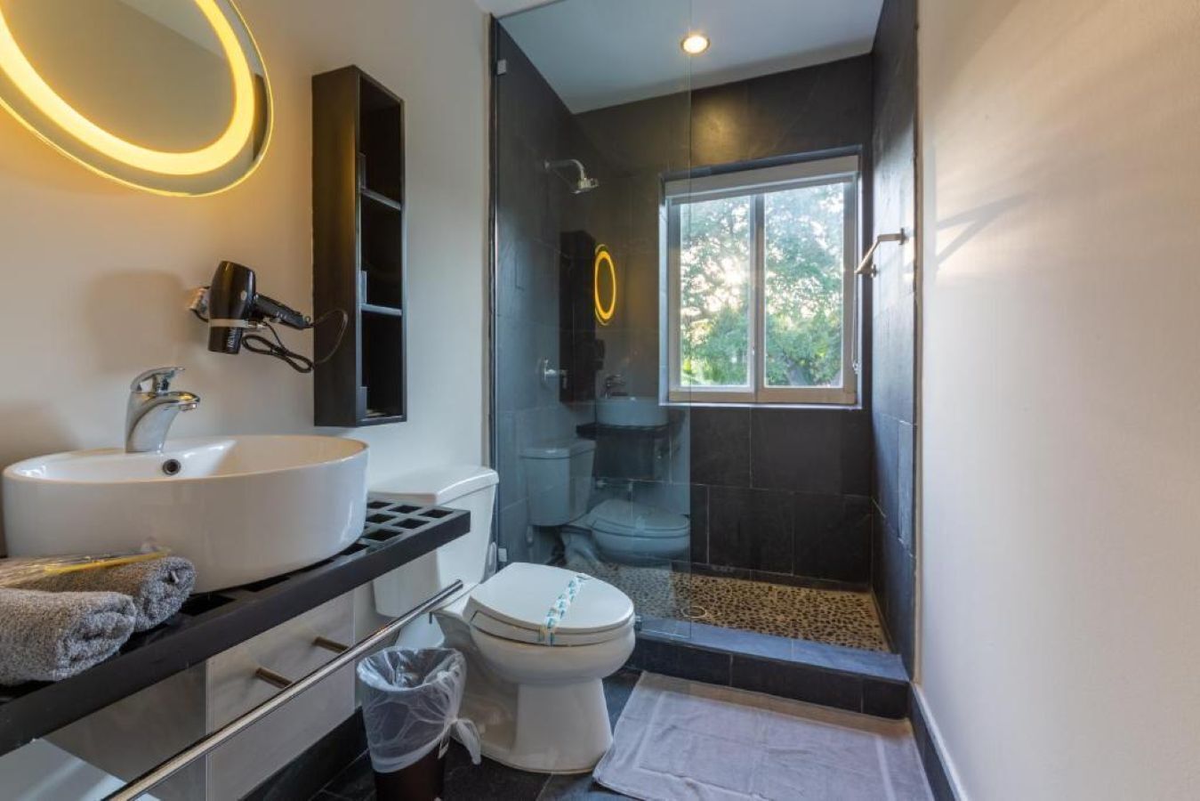 A modern bathroom with a white sink, a toilet, a glass shower enclosure, and a window providing natural light.