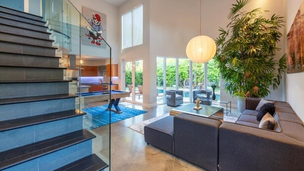 A modern interior with a staircase, a seating area, and a large plant. - Villa II Palazzo by Glam Homes (North Miami)