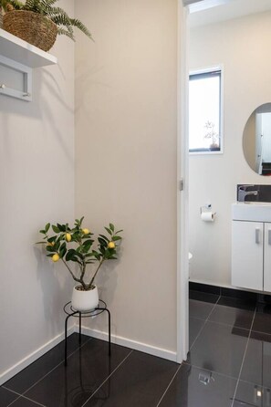 A hallway with a potted plant, a white shelf, and a doorway leading to a bathroom with a toilet and a mirror. - Riccarton Family Stay Near Mall & Uni (Christchurch)