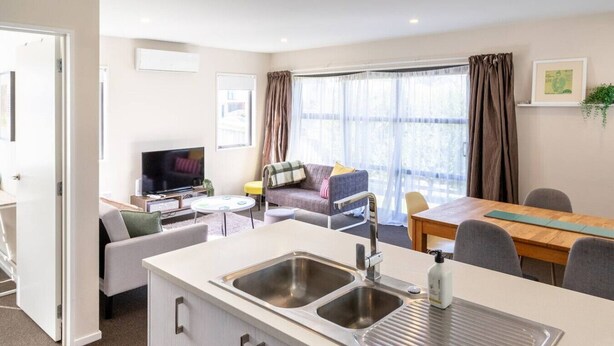 Una habitación de hotel moderna con kitchenette, sofá, televisor y comedor.