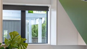 Eine moderne Küche mit einer zentralen Kochinsel, Barhocker, einer Kaffeemaschine und einem Fenster mit Blick ins Grüne.