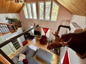 Una habitación estilo loft con techo de madera, una escalera, un sofá, una silla roja, un televisor y una gran estatua de toro.