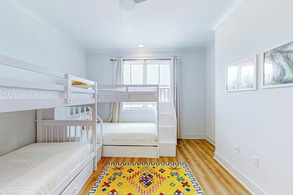 A room with bunk beds, a window with curtains, and a patterned rug.