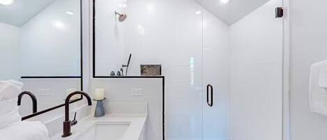 Un baño moderno con cabina de ducha de vidrio, lavabo blanco y espejo.