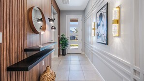 A hallway with a wooden wall, a mirror, pendant lights, a potted plant, a framed picture, and a door with windows. - 6BR/4.5BA Luxury Disney Decor w/ Pvt Pool & Resort (Kissimmee)
