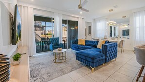 A spacious living area with a blue sofa set, a round coffee table, and a ceiling fan. - 6BR/4.5BA Luxury Disney Decor w/ Pvt Pool & Resort (Kissimmee)