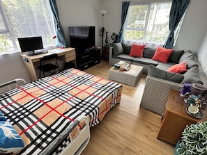 A furnished room with a bed, a desk with a computer, a sofa, a coffee table, and a television.