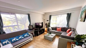 Ein modernes Wohnzimmer mit einer Couch, einem Schlafsofa, einem kleinen Tisch, einem Fernseher und einem Ventilator.