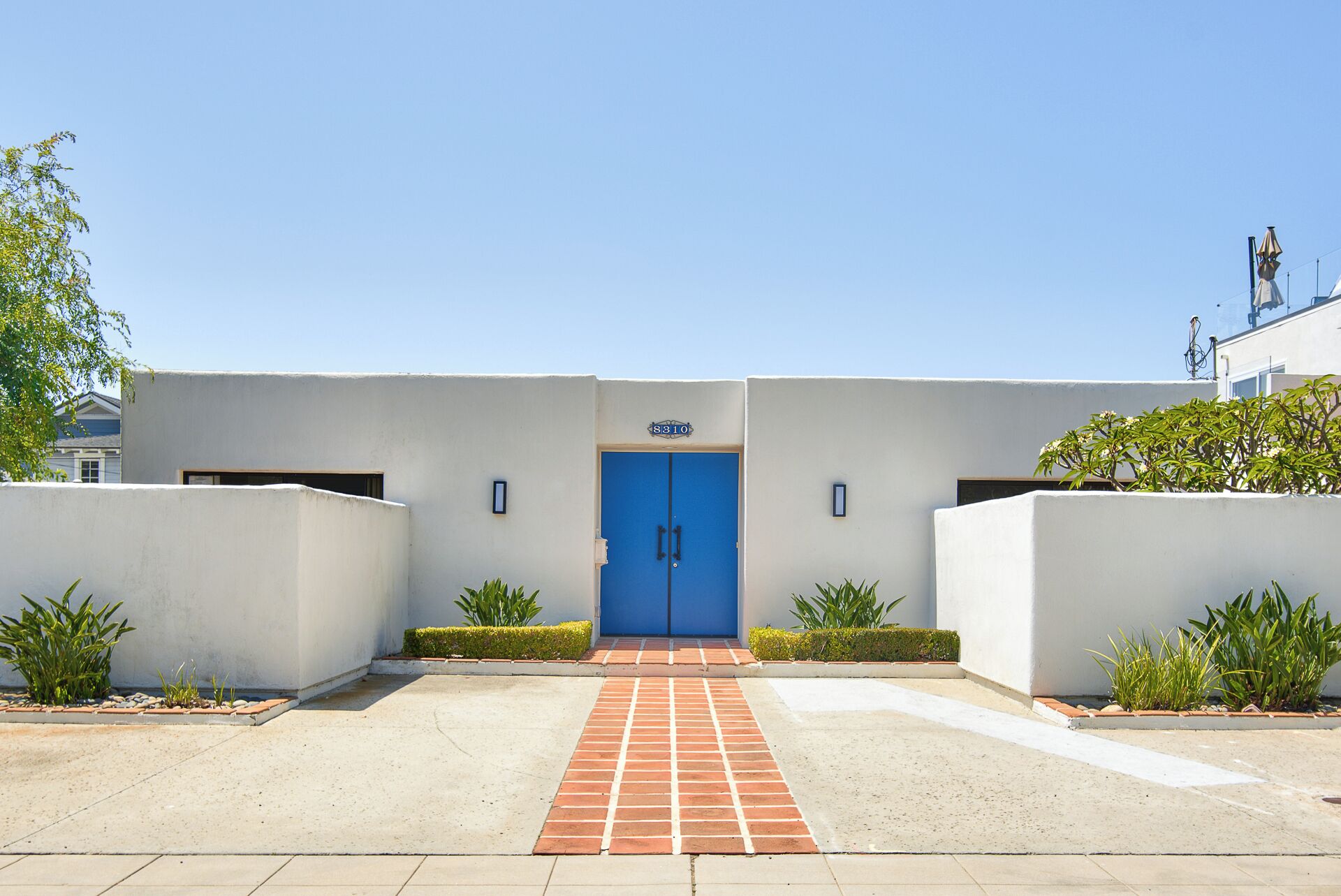 Un bâtiment avec une porte bleue, un panneau indiquant le numéro au-dessus, et une entrée pavée.