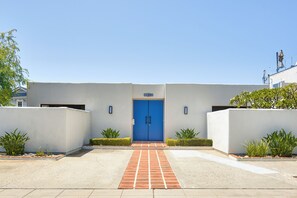 Un edificio con una puerta azul, un cartel con un número encima y un acceso pavimentado.