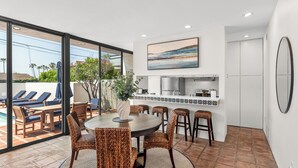 A modern kitchen with a tiled backsplash, a dining area with wicker chairs, and a large window overlooking a pool area. - New! La Jolla Shores 2BD with Pool- Walk to Beach! (La Jolla)