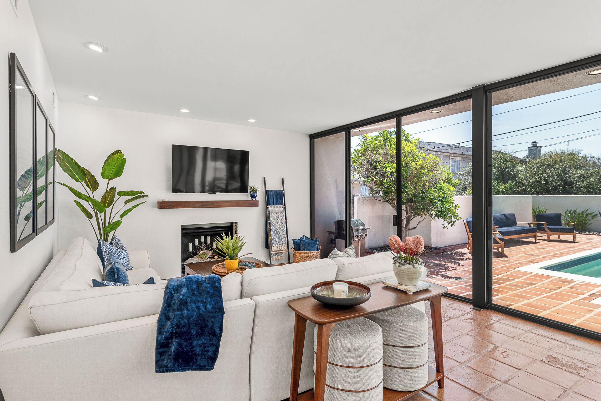 A modern living room with a fireplace, a flat-screen TV, and a large sliding glass door leading to a patio with outdoor furniture.