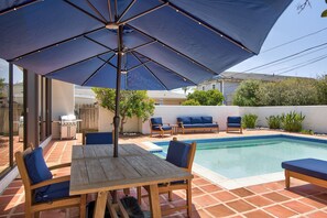 Un patio con piscina, mobiliario exterior y una parrilla.