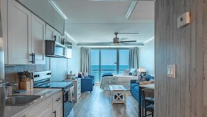 Een moderne keuken met een inbouwoven en magnetron, een eetgedeelte met tafel en stoelen, en een woonkamer met bank en uitzicht op zee.