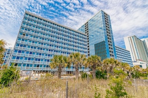 A modern hotel with a glass facade, palm trees, and a clear sky. - Yachtsman South Tower 803A Studio (Myrtle Beach)