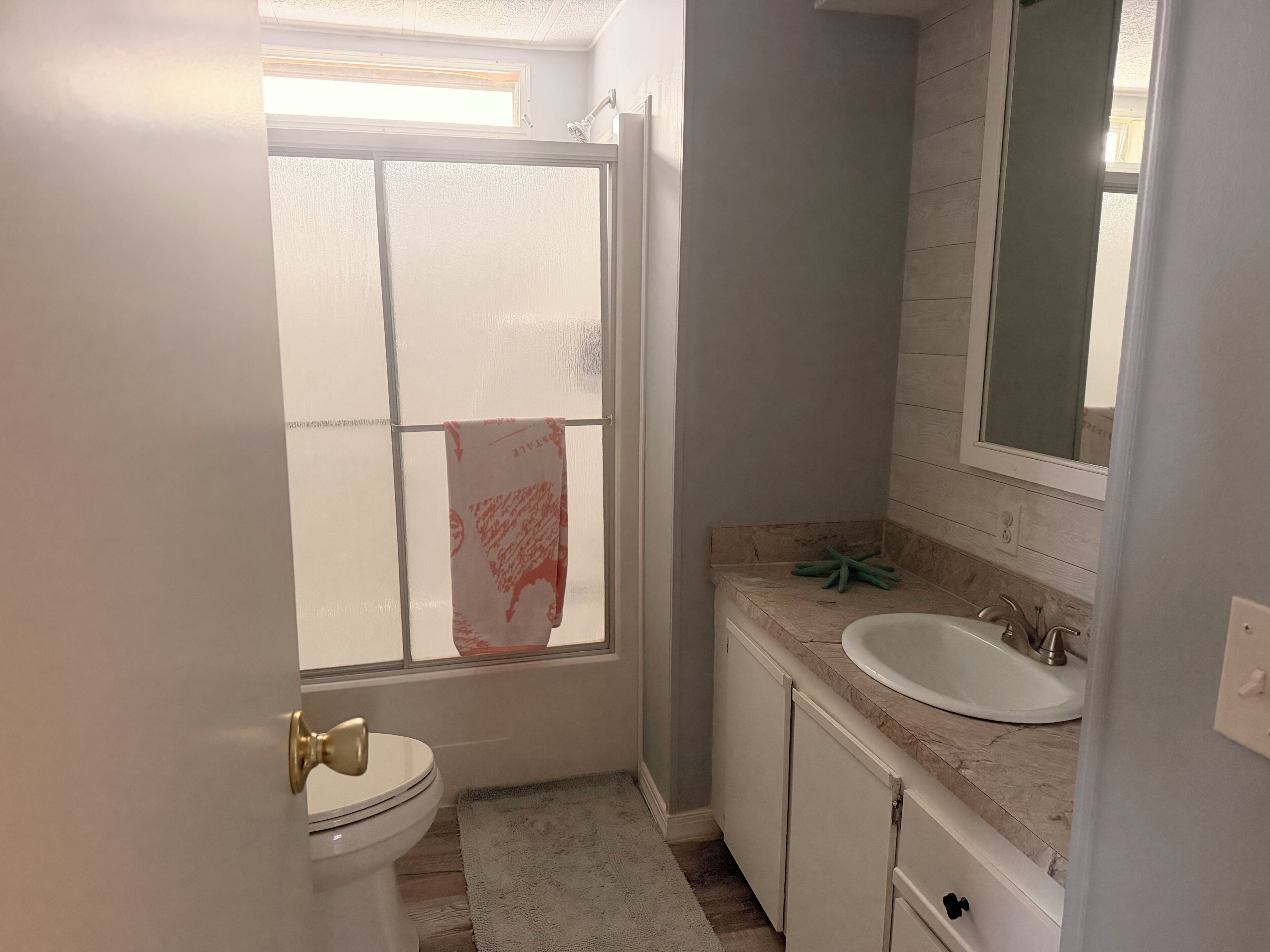 A bathroom with a toilet, sink, mirror, and a window with frosted glass.