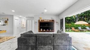 Ein modernes Wohnzimmer mit einem grauen Ecksofa, einem Kamin mit einem Schild mit dem Schriftzug 'home' und Blick auf einen Poolbereich.