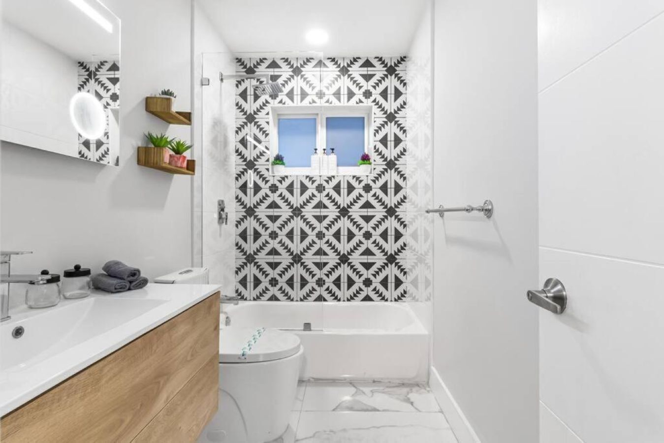 Ein modernes Badezimmer mit Badewanne, Toilette, Waschtisch mit Spiegel und gemusterten Fliesen.