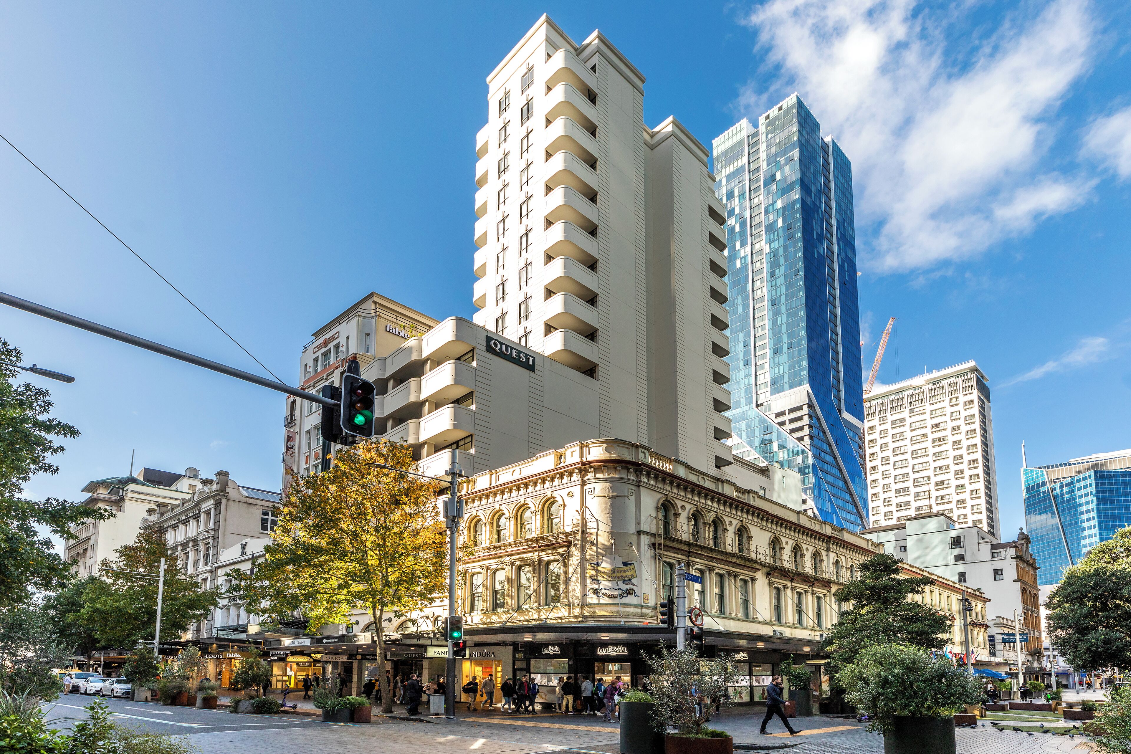 A historic building with a 'QUEST' sign, surrounded by modern skyscrapers.