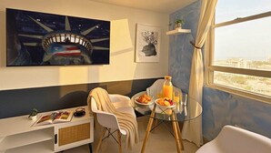 A modern room with a large painting, a glass table with breakfast, a sofa, and a view of the city. - Elevate Your Stay! Prime 2 Beds Home w Ocean View! (San Juan)