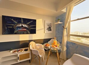 A modern room with a large painting, a glass table with breakfast, a sofa, and a view of the city. - Elevate Your Stay! Prime 2 Beds Home w Ocean View! (San Juan)
