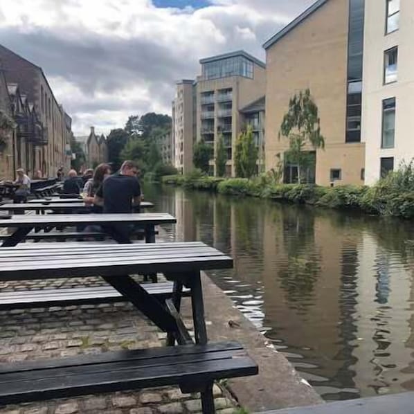 Outdoor seating by a canal with buildings in the background.