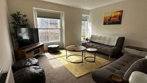Een woonkamer met een televisie, bank, salontafel en een schilderij aan de muur.