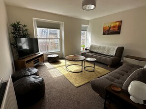 A living room with a TV, sofa, coffee table, and a painting on the wall. - The Joseph Cosy at Lancaster (Lancaster)