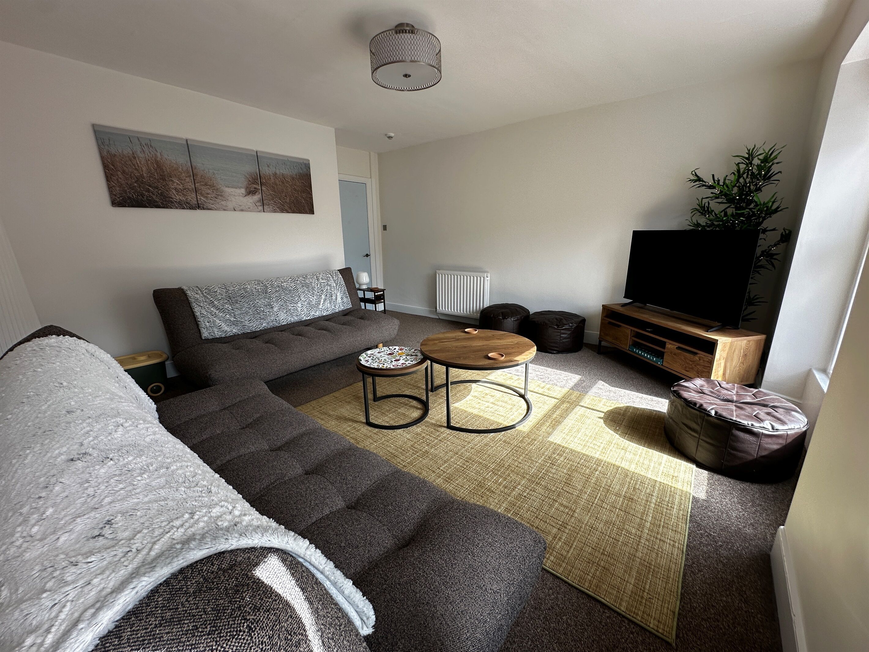 A modern living room with a sectional sofa, a round coffee table, a flat-screen TV, and a small side table.
