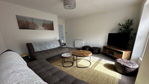 Een moderne woonkamer met een modulaire bank, een ronde salontafel, een flatscreen-televisie en een bijzettafeltje.