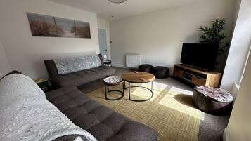 A modern living room with a sectional sofa, a round coffee table, a flat-screen TV, and a small side table.