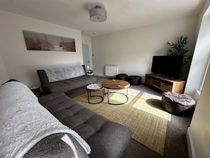 A modern living room with a sectional sofa, a round coffee table, a flat-screen TV, and a small side table.