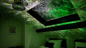 Een kamer met een bed, een hanglamp en een wandprojectie van een groene nevel.