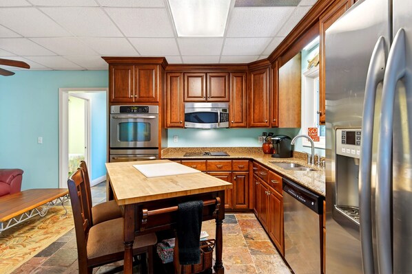 Una cocina con armarios de madera, electrodomésticos de acero inoxidable, encimera de granito y comedor con mesa y sillas.