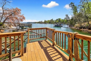 A wooden deck with a view of a river, boats, and a bridge. - Paddle On Inn | Spacious Lakefront Retreat with Private Dock + VIEWS! (Nebo)