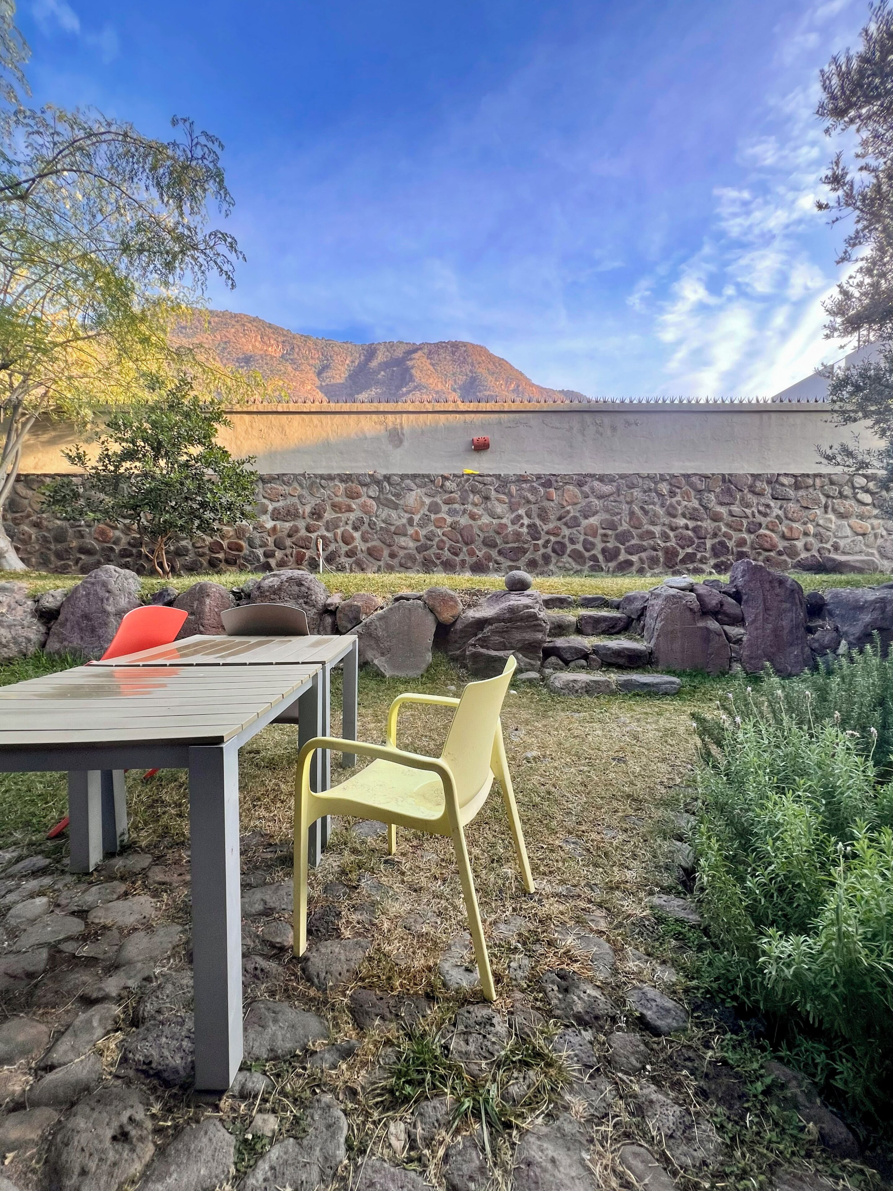 An outdoor seating area with a table and chairs, a stone wall, and a view of a mountain range.
